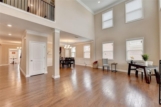 living room featuring ornate columns, wood-type flooring, ornamental molding, a notable chandelier, and a high ceiling