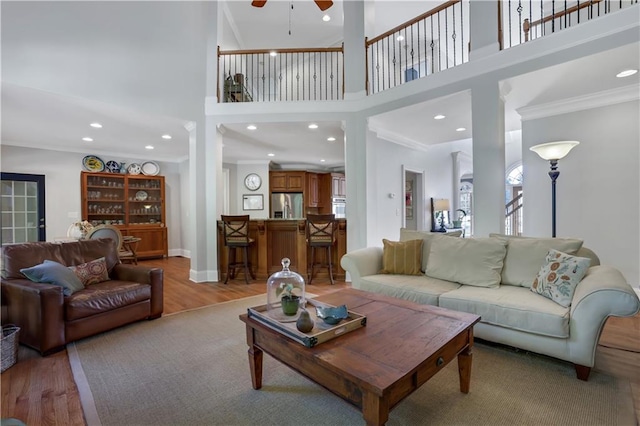 living room featuring crown molding, a towering ceiling, ceiling fan, and light hardwood / wood-style floors