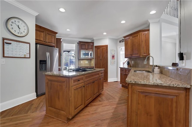 kitchen featuring sink, crown molding, stainless steel appliances, a center island, and light stone counters