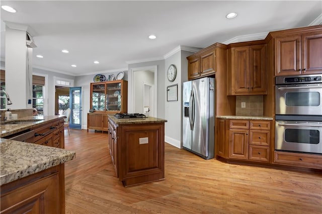 kitchen with sink, stainless steel appliances, tasteful backsplash, light stone countertops, and light wood-type flooring