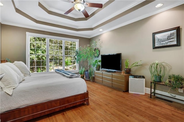 bedroom featuring crown molding, a tray ceiling, light hardwood / wood-style flooring, and ceiling fan