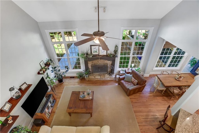 living room with wood-type flooring, a stone fireplace, plenty of natural light, and ceiling fan