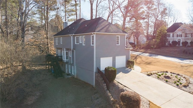 view of side of property featuring driveway, a chimney, and an attached garage