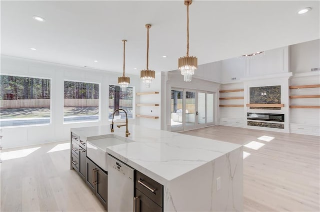 kitchen featuring dishwasher, sink, hanging light fixtures, light stone countertops, and an island with sink