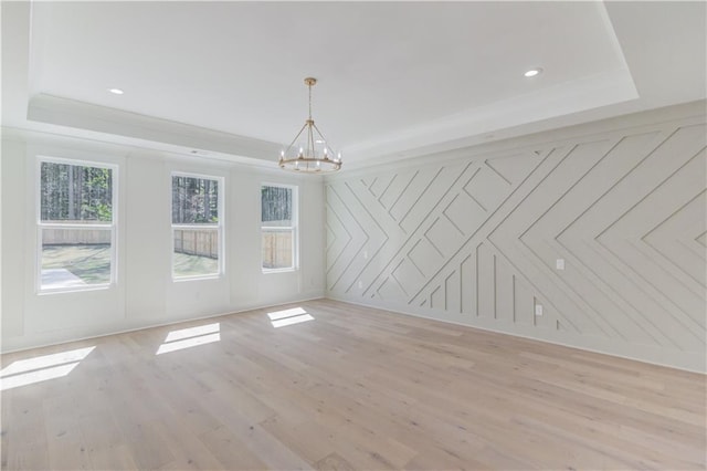 unfurnished room featuring light hardwood / wood-style floors, a raised ceiling, and a chandelier