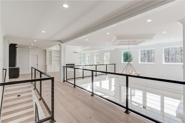 hall featuring built in shelves, an inviting chandelier, a raised ceiling, crown molding, and light wood-type flooring