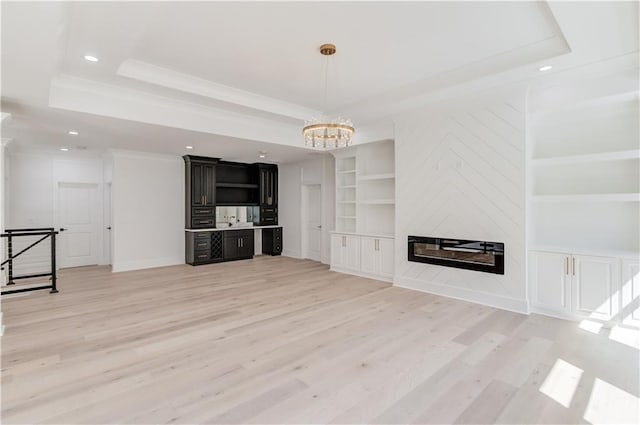 unfurnished living room featuring built in shelves, a large fireplace, light hardwood / wood-style flooring, a notable chandelier, and a tray ceiling