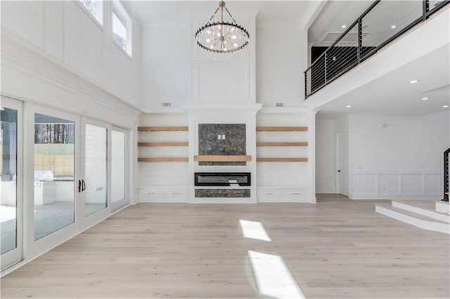 unfurnished living room featuring light hardwood / wood-style flooring, a fireplace, a high ceiling, and an inviting chandelier