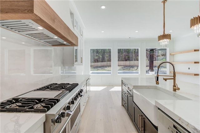 kitchen with white cabinetry, sink, hanging light fixtures, light stone counters, and custom exhaust hood