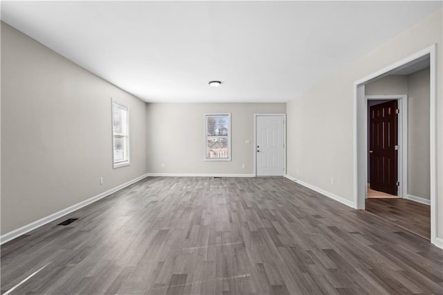 unfurnished living room featuring visible vents, baseboards, and dark wood-style flooring