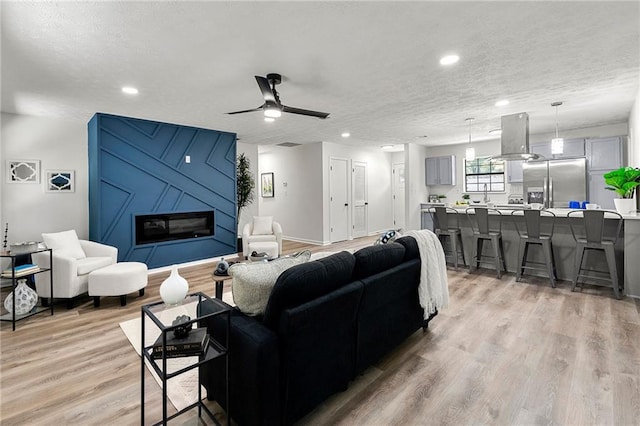 living room with ceiling fan, a textured ceiling, and light hardwood / wood-style flooring