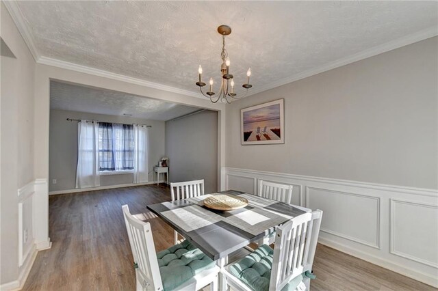 dining space with an inviting chandelier, a textured ceiling, crown molding, and hardwood / wood-style floors