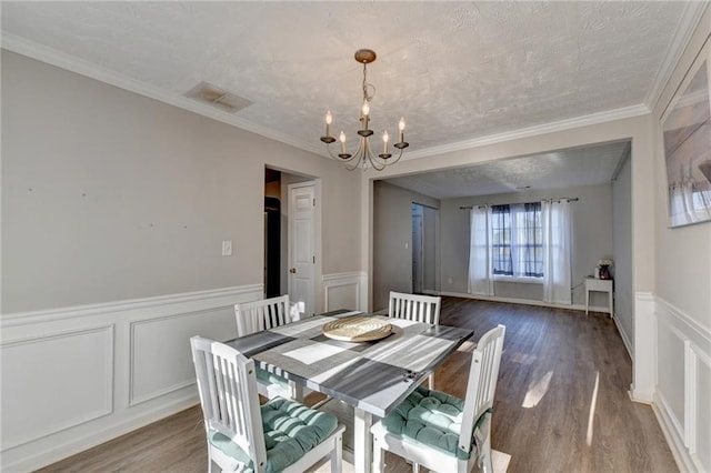 dining area with a textured ceiling, crown molding, an inviting chandelier, and hardwood / wood-style floors