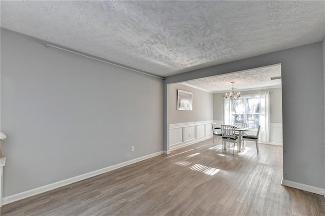 unfurnished dining area with a textured ceiling, wood-type flooring, and an inviting chandelier