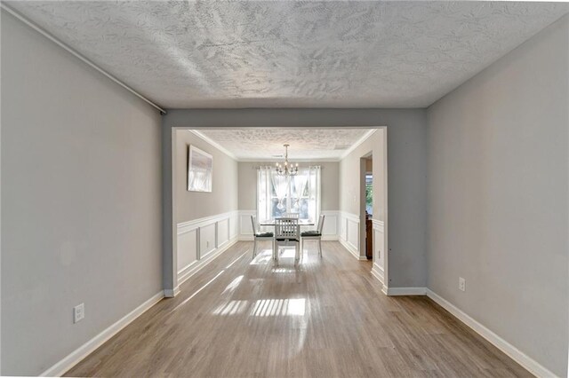 unfurnished dining area with a textured ceiling, an inviting chandelier, and hardwood / wood-style floors