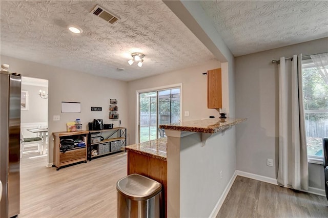 kitchen featuring a breakfast bar, a textured ceiling, light hardwood / wood-style floors, kitchen peninsula, and stainless steel fridge