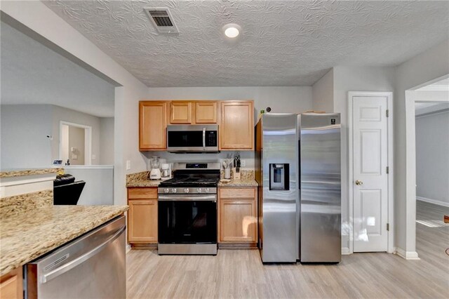 kitchen featuring appliances with stainless steel finishes, a textured ceiling, light wood-type flooring, and light stone countertops