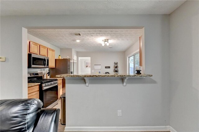 kitchen featuring light stone counters, a textured ceiling, a breakfast bar area, kitchen peninsula, and appliances with stainless steel finishes