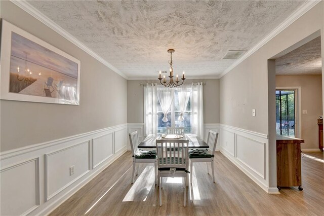 dining area with a notable chandelier, light hardwood / wood-style flooring, crown molding, and a textured ceiling