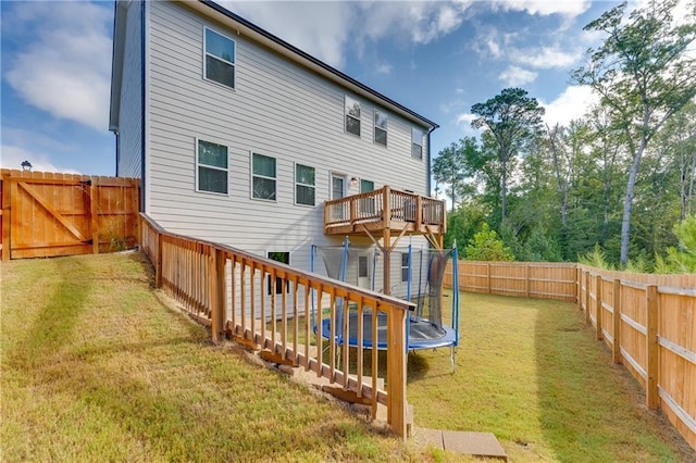 rear view of property featuring a wooden deck, a trampoline, and a lawn