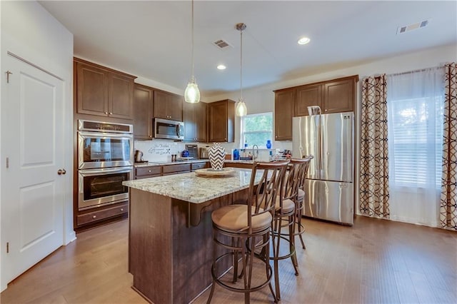 kitchen featuring appliances with stainless steel finishes, hanging light fixtures, a kitchen bar, light stone counters, and a kitchen island