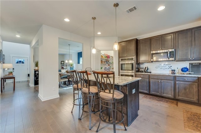 kitchen with a breakfast bar area, hanging light fixtures, a center island, light stone counters, and stainless steel appliances