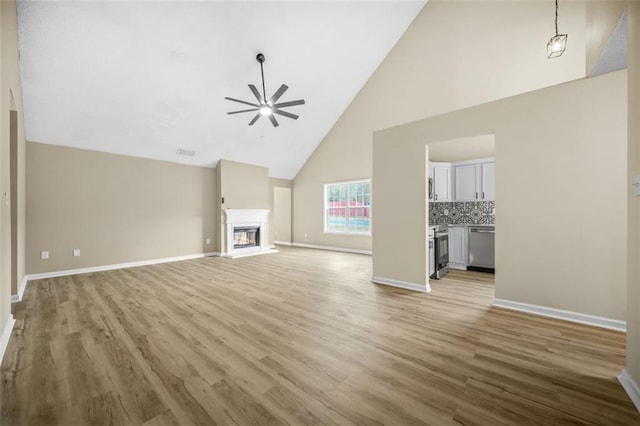 unfurnished living room with a glass covered fireplace, baseboards, ceiling fan, and light wood finished floors