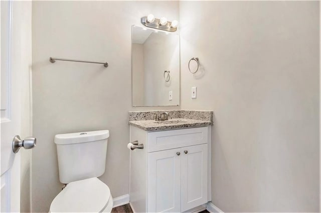 half bathroom featuring toilet, vanity, and baseboards