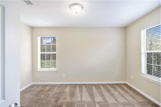 spare room featuring visible vents, carpet floors, a textured ceiling, and baseboards