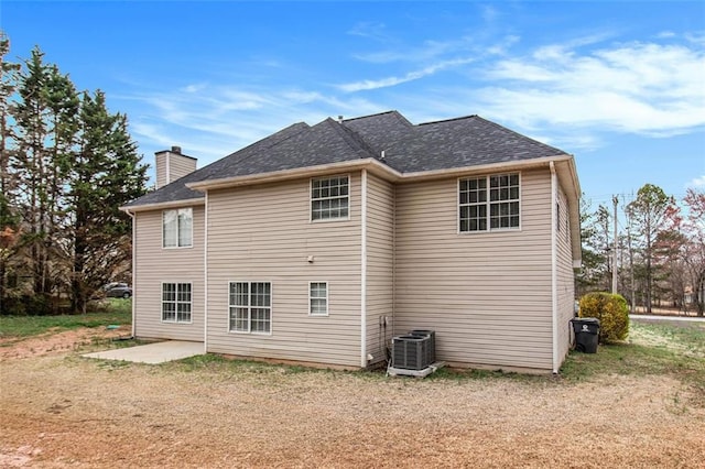 rear view of property featuring cooling unit, roof with shingles, and a chimney