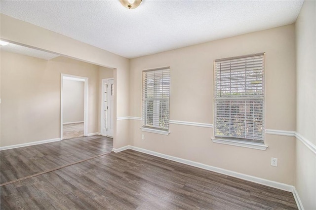 empty room featuring a textured ceiling, baseboards, and wood finished floors