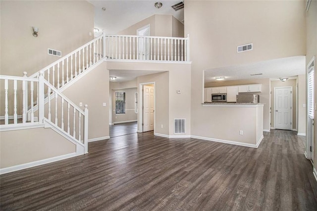 unfurnished living room with dark wood finished floors, visible vents, and stairway