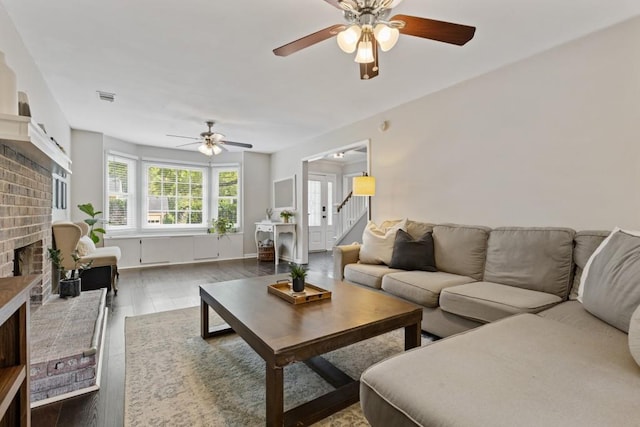 living room with a brick fireplace, dark hardwood / wood-style floors, and ceiling fan