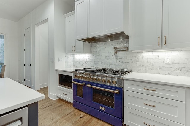 kitchen featuring tasteful backsplash, white cabinetry, built in microwave, range with two ovens, and light wood-type flooring