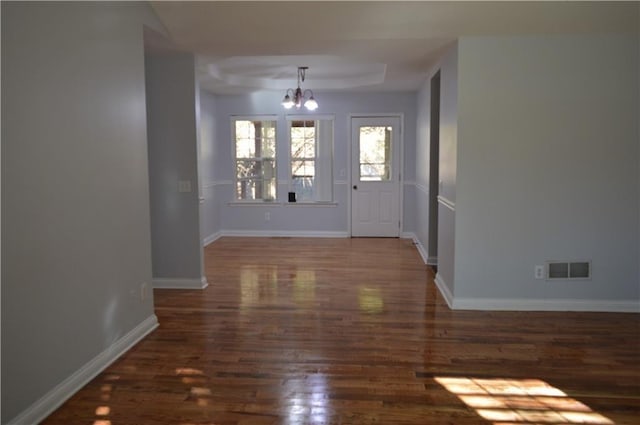 interior space featuring a raised ceiling, dark wood-type flooring, and an inviting chandelier