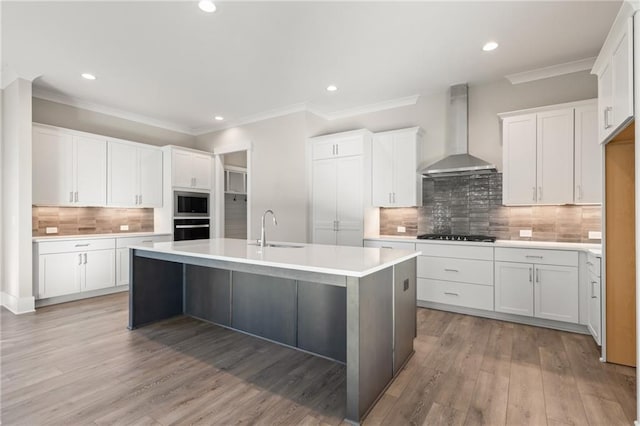 kitchen with white cabinets, a center island with sink, sink, wall chimney exhaust hood, and wall oven