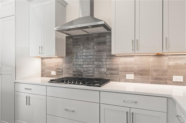 kitchen featuring wall chimney exhaust hood, white cabinetry, decorative backsplash, and stainless steel gas cooktop