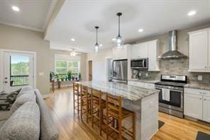 kitchen with white cabinetry, wall chimney exhaust hood, stainless steel appliances, and a kitchen island