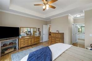 bedroom featuring hardwood / wood-style floors, ensuite bathroom, a raised ceiling, ceiling fan, and ornamental molding