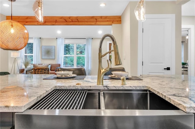 kitchen featuring decorative light fixtures, light stone counters, a wealth of natural light, and sink