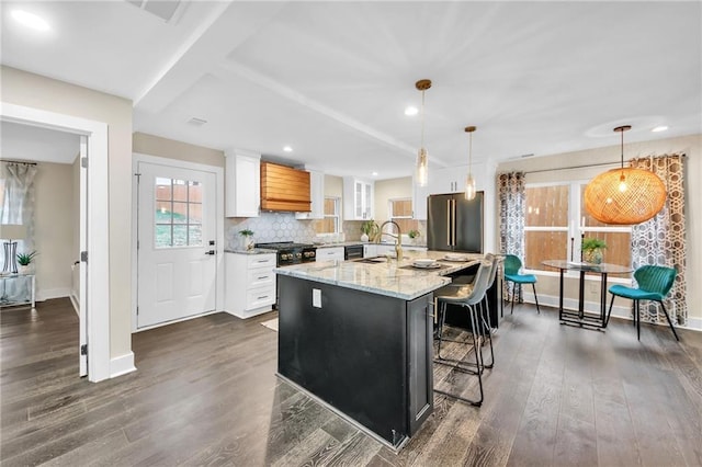 kitchen with white cabinets, decorative light fixtures, a center island with sink, and light stone counters