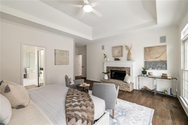 bedroom with visible vents, a tray ceiling, dark wood finished floors, and a stone fireplace