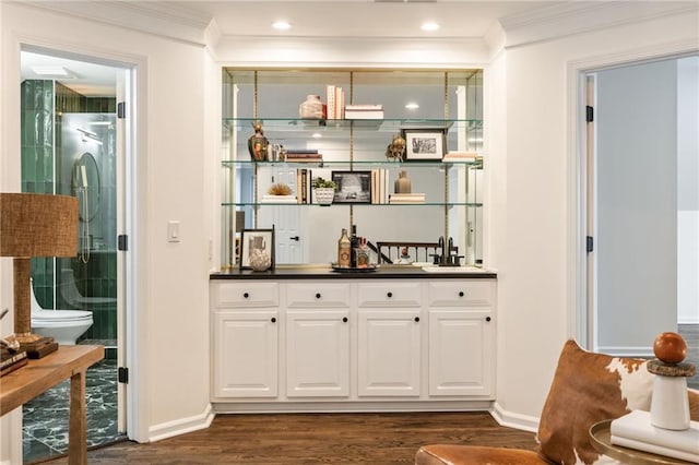 bar featuring crown molding, dark wood-type flooring, baseboards, and wet bar