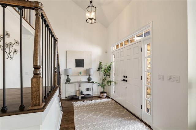 foyer with dark wood-type flooring, high vaulted ceiling, baseboards, and an inviting chandelier