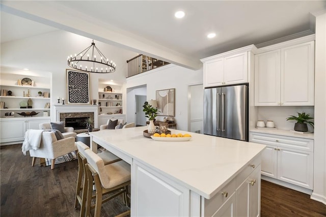 kitchen featuring high end refrigerator, a kitchen island, a fireplace, white cabinetry, and beamed ceiling