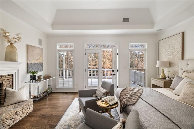 bedroom with a stone fireplace, visible vents, access to outside, a raised ceiling, and dark wood finished floors