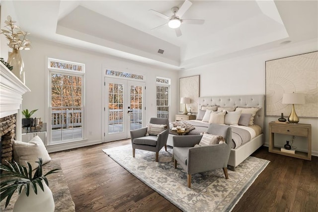 bedroom featuring access to exterior, a tray ceiling, french doors, and a stone fireplace