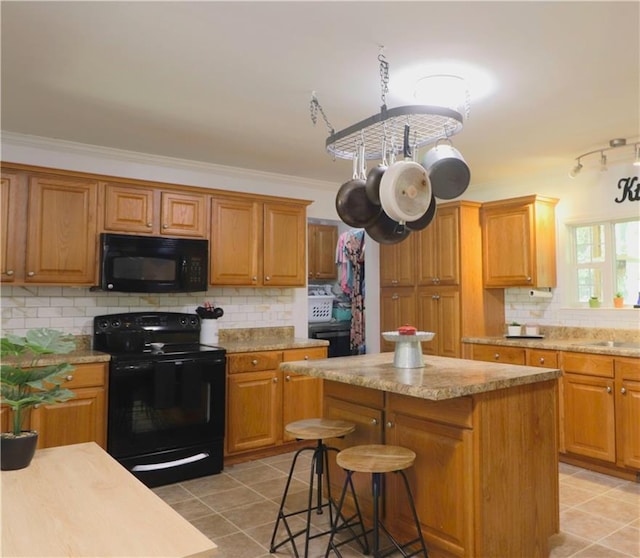 kitchen with a center island, light tile patterned floors, backsplash, ornamental molding, and black appliances