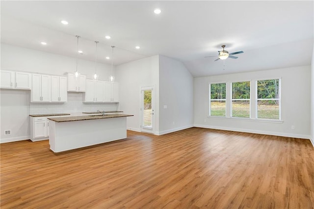 kitchen with white cabinetry, hanging light fixtures, an island with sink, ceiling fan, and backsplash