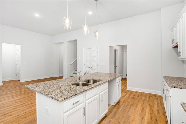 kitchen with sink, white cabinets, hanging light fixtures, a kitchen island with sink, and light wood-type flooring